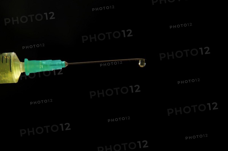 Syringe with needle with a drop of liquid coming out, isolated on black background and copy space