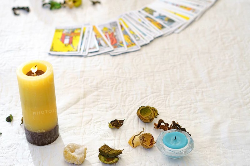 Table of a fortune teller with tarot cards, candles, quartz stones, crystal ball on a white tablecloth