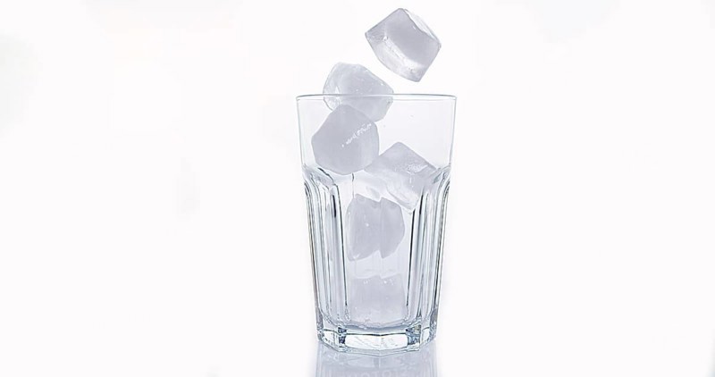 Ice Cubes Falling into Glass against White Background