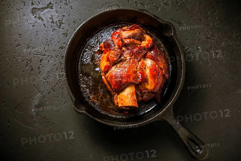 Traditional German cuisine - Roasted pork knuckle eisbein (Schweinshaxe) in iron pan on black background