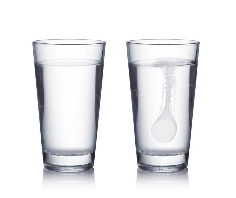 Glass with effervescent tablet in water with bubbles on white background