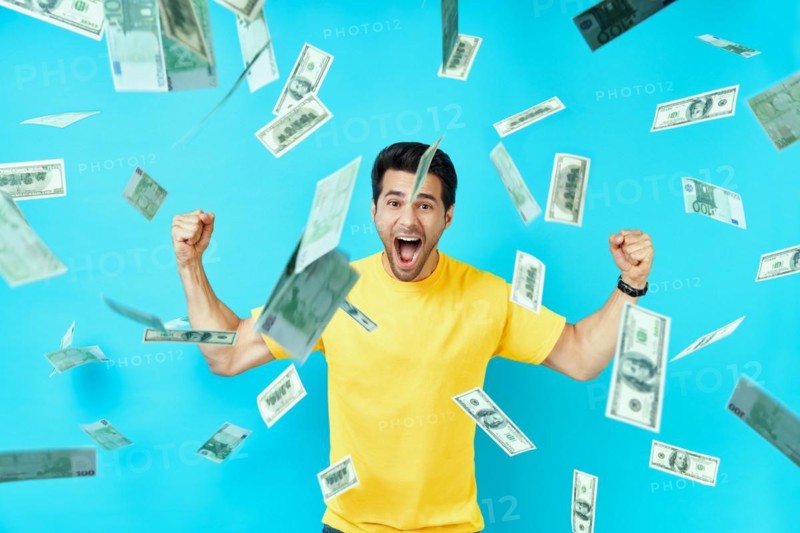 Happy excited man standing under money rain banknotes falling down. Success, business, and fortune concept