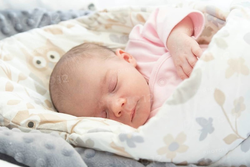 Sleeping newborn baby. Cute little girl one week old at home. Adorable lying on side covered with blanket. No retouch, newborn dry skin