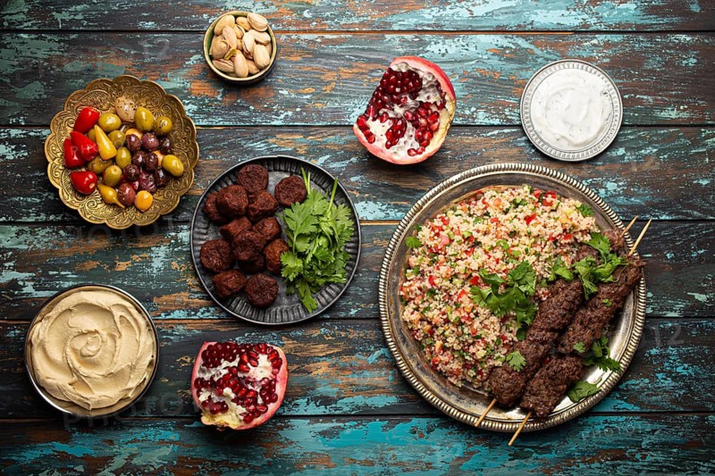 Various Turkish dishes: meat kebab with tabbouleh salad, falafel, hummus, olives, pistachios and other Middle Eastern meze on wooden table top view. Ethnic arab food, cuisine of Turkey