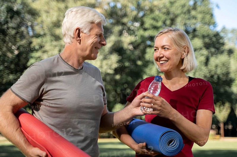 Smiley older couple outdoors with yoga mats water bottle