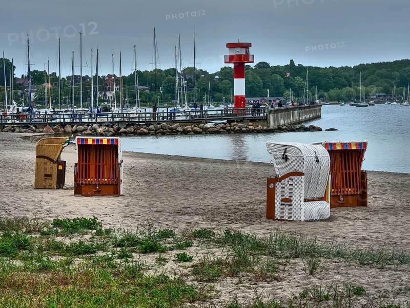 Beach with beach chairs, in the background a lighthouse and boats, overcast sky, eckernförde, schleswig-holstein, germany