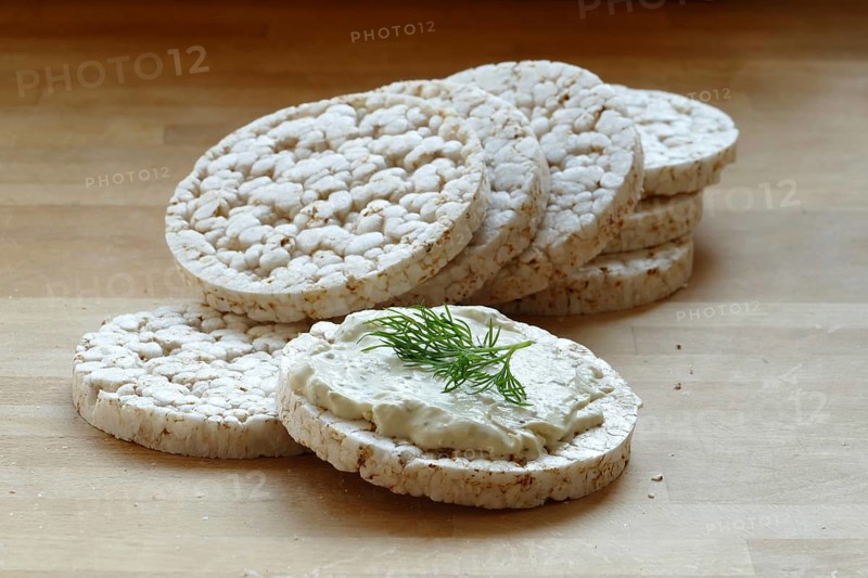 Group of rice cakes, one with cream cheese and herbs on a wooden board
