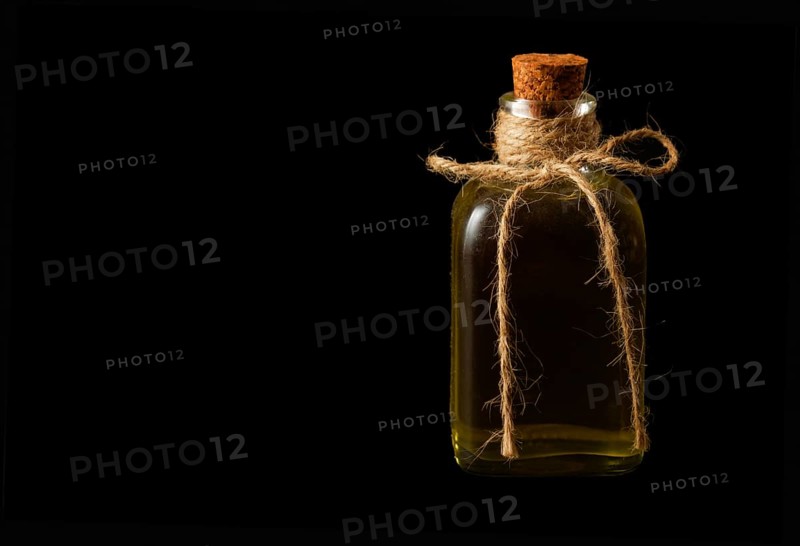 Close-up of a glass bottle with olive oil and cork stopper isolated on a black background