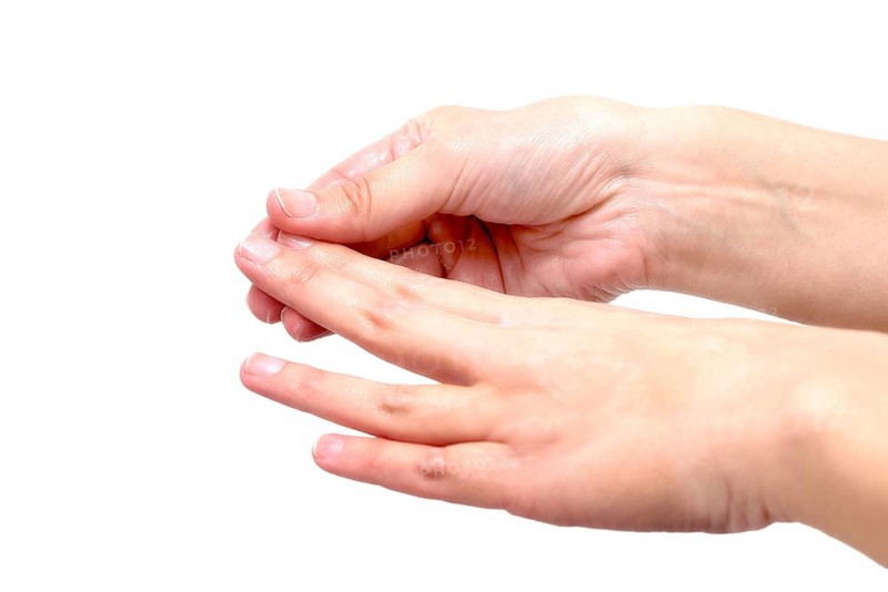 Close-up of female hands while applying moisturizing lotion in order to repair damaged and dry skin, on grey background