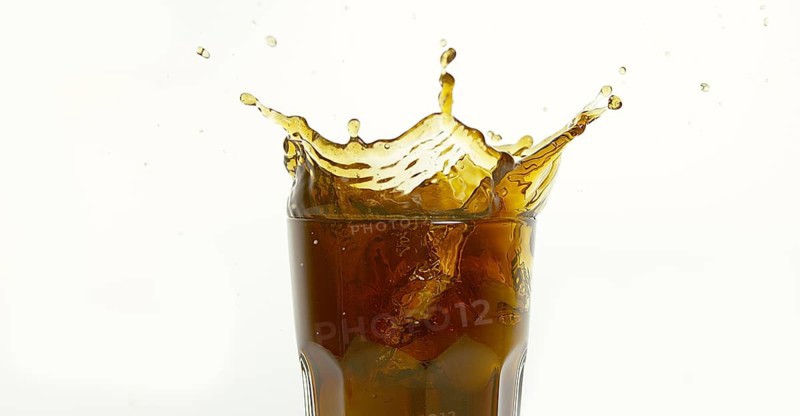 Ice Cubes Falling into Glass of Coke against White Background