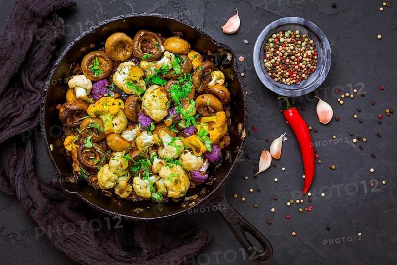 Roasted mushrooms and cauliflower, with onion, garlic and herbs in pan on black background