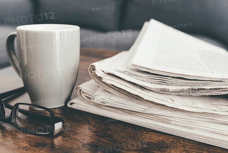 close-up shot of stack of newspapers, coffee mug and glasses on living room table