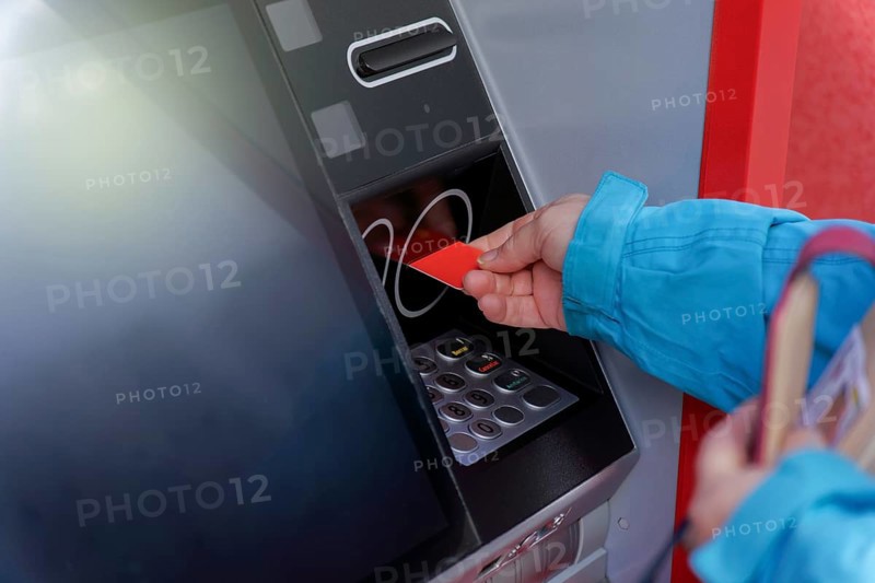 Woman in blue jacket inserting her credit card into an ATM to withdraw cash