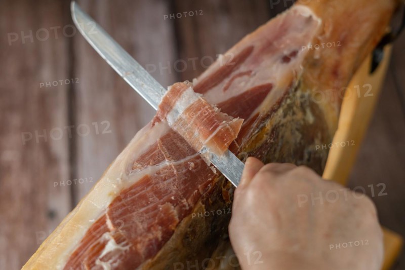 Spanish acorn-fed iberian ham close-up open knife cut by the hands of a charcuterie woman