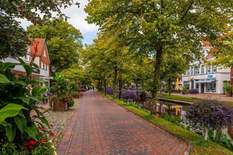 A paved path next to a canal, flanked by lush plants and residential buildings, Papenburg, Emsland, Lower Saxony