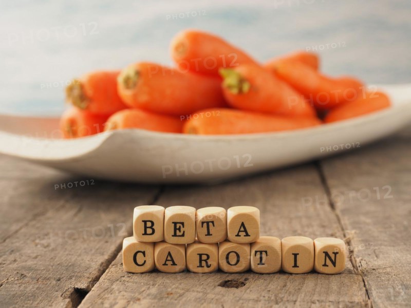 Wooden dices with the German words beta carotene and fresh carrots in the back, healthy eating concept