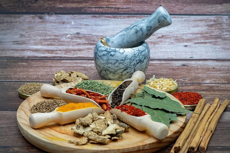 Different types of spices in wooden spoons on a wooden disk ginger, cayenne, pepper, cinnamon, parsley, bay leaf, aniseed