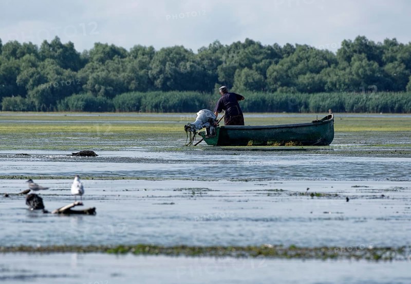 Fishermen in a boat on the water of Lacul Isaccel, a lake in the Danube Delta. UNESCO Danube Delta Biosphere Reserve. Munghiol, Tulcea, Romania, Southeast Europe, Europe