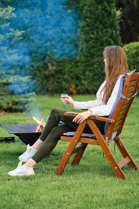 Young woman resting in lounge chair on backyard next to a barbecue, view on profile