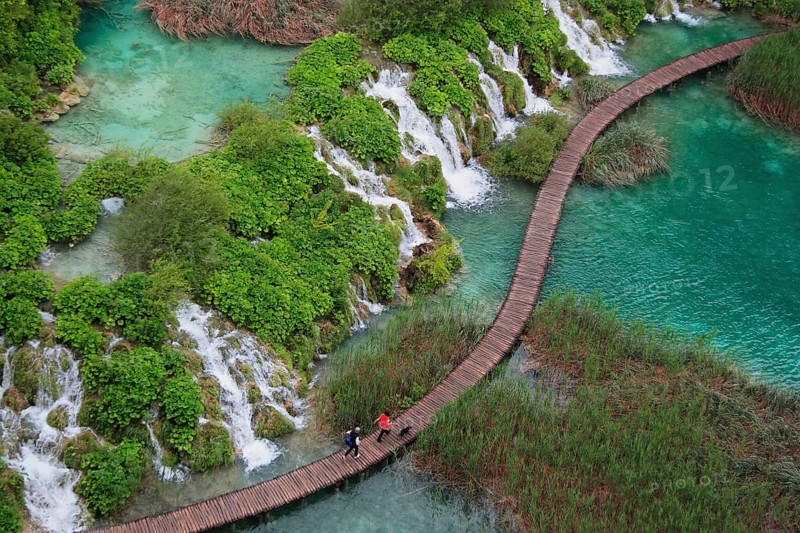 Wooden footbridge with hikers over turquoise ponds and waterfalls at Plitvice Lakes, Croatia, Europe