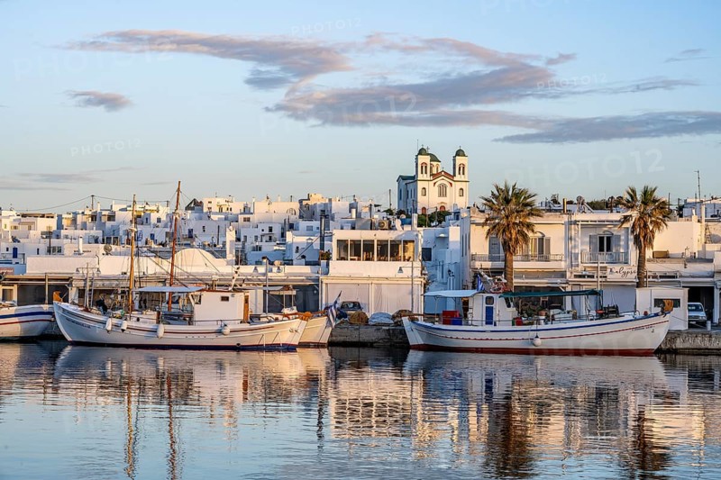 View of Naoussa, Fishing boats in the harbour at sunset, reflected in the sea, White Cycladic houses and church Agios Faneromeni, Naoussa, Paros, Cyclades, Greece, Europe