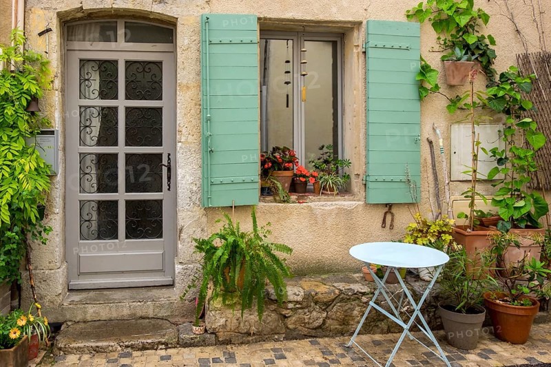 An old house façade with green shutters, numerous plants and a small round table, Vauvenargues, Provence-Alpes-Cote d'Azur, France, Europe