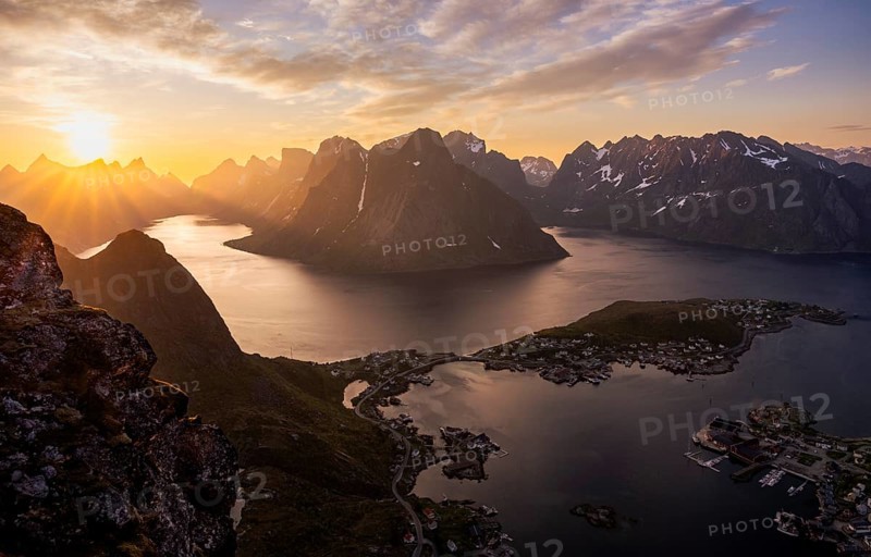 Mountain landscape, view from Reinebringen mountain to the village of Reine and Gravdalsbukta (Gravdals Bay), Olstinden mountain in the centre, Lilandstinden mountain on the right. On the left the Reinefjord with other mountains. At night at the time of the midnight sun in good weather. The sun is above the mountains. Early summer. Reine, Moskenesoya, Lofoten, Norway, Europe
