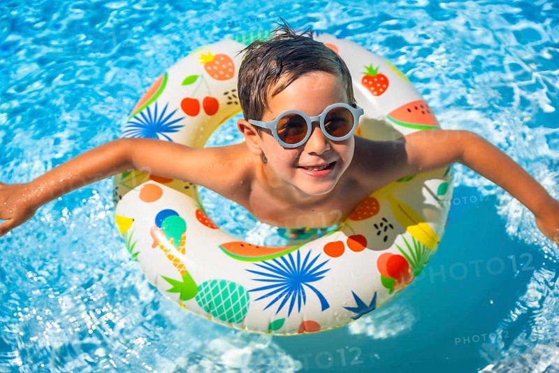 Top view of a happy young boy inside a blue swimming pool with swim goggles and a float