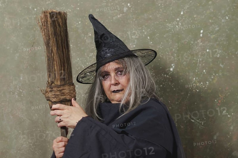 Old witch with white hair and a black hat with an ancient broom in her hands