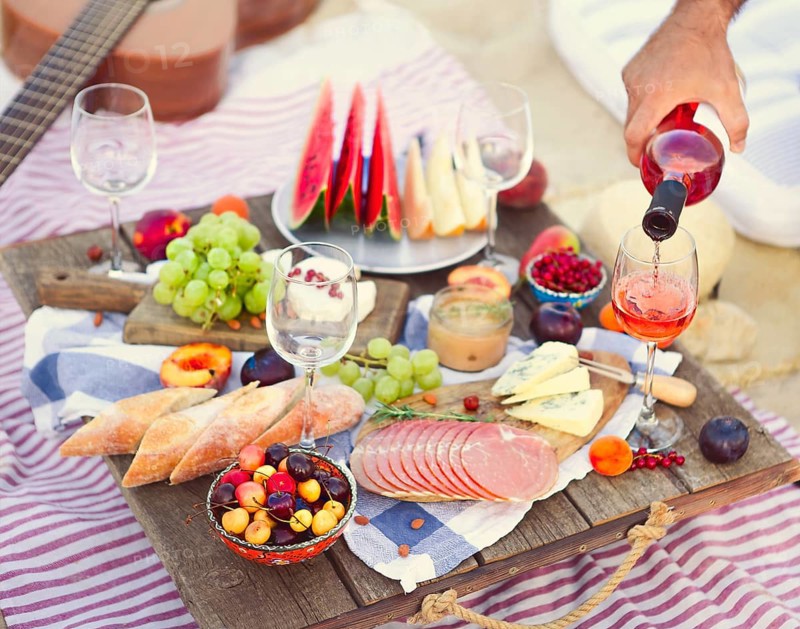 Crop male serving pink wine having picnic with delicious snacks and fruit on sandy beach