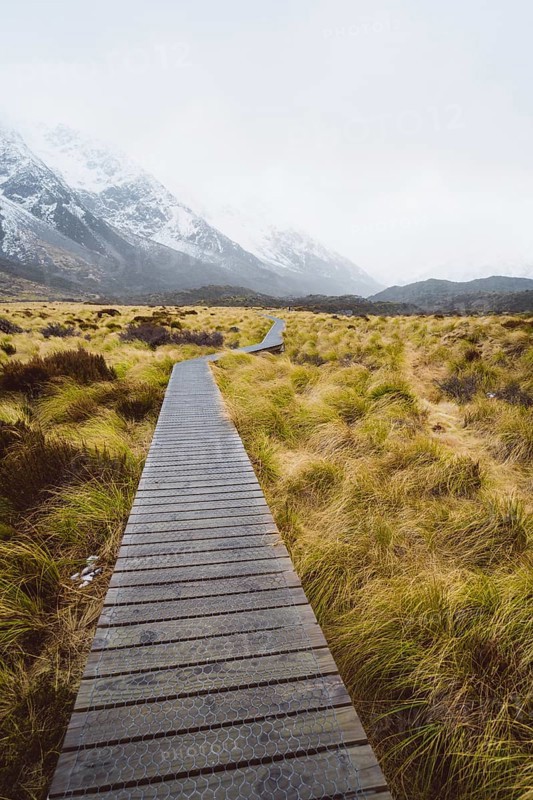 Wooden walkway through a landscape surrounded by grass with snow-capped mountains in the background, Hooker Valley Track, New Zealand, Oceania