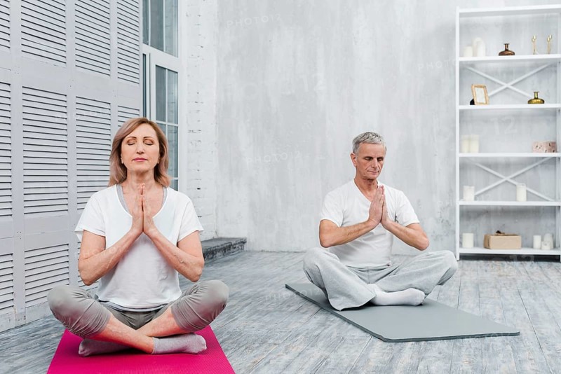 Senior couple meditating with praying hands yoga mat home