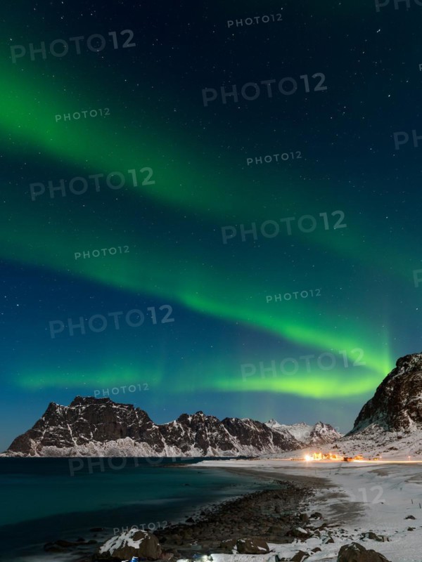Spectacular dancing green strong northern lights over the famous round boulder beach near Uttakleiv on the Lofoten islands in Norway on clear winter night with snow-clad mountains
