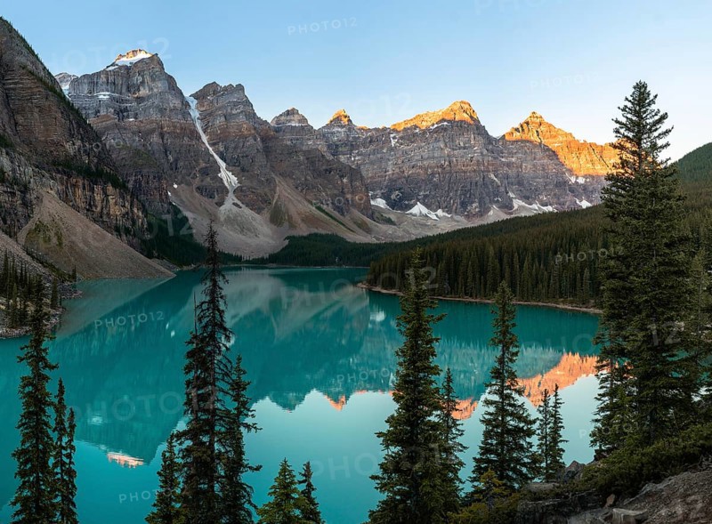Sunset over a serene lake surrounded by rocky mountains and pine trees, with reflections in the clear water, Moraine Lake, Banff National Park, Canadian Rockies