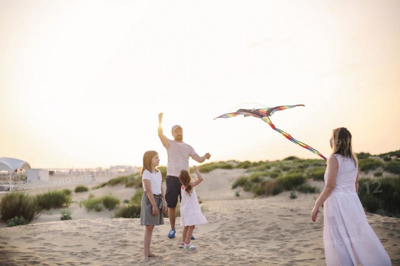 Happy family with parents and kids playing together with snakes on a beach vacation. Summer happiness concept with Mixed-race people having fun by the sea