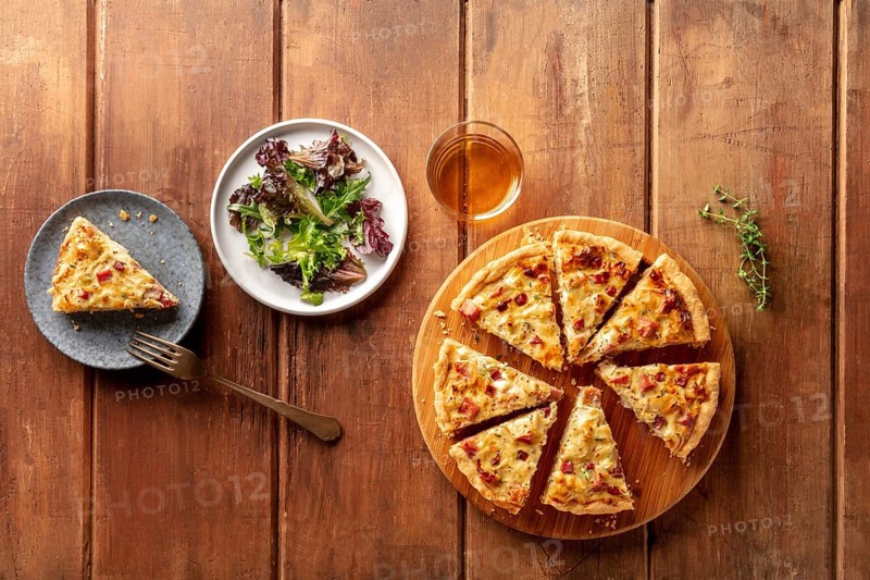 An overhead photo of a quiche with wine and mesclun salad leaves on a dark rustic wooden background with copy space