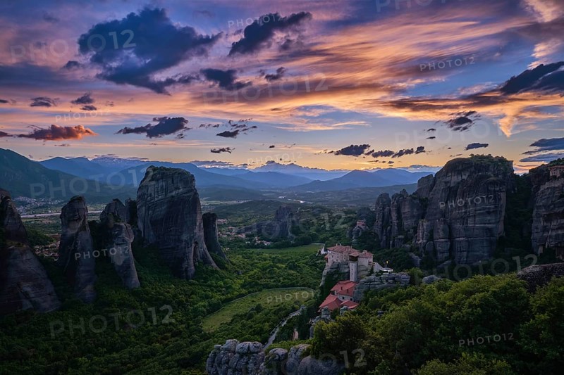 Twilight view of Meteora valley. Valley in last moments of sunlight, hazy distant mountains, clifftop Moni Agias Varvaras Roussanou nunnery and rocks and cliffs. Beautiful sky in sunset colors, colorful clouds. Greece, UNESCO World Heritage
