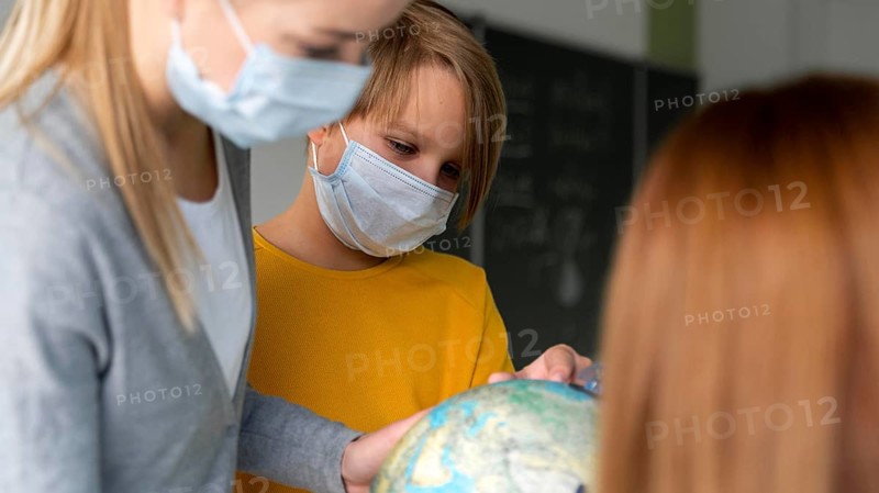 Female teacher with medical mask teaching geography with globe classroom