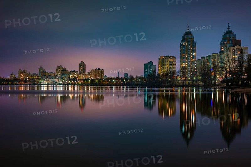 Night view of modern buildings in the Obolon district of Kiev, Ukraine, close to the Dnieper River, The lights reflect on the calm water, Europe