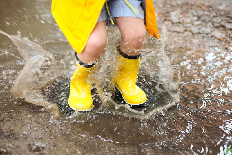 Little girl wearing yellow boots and coat jumping in rainy day