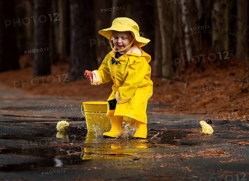 A small child plays in the rain while little chicks try to get a drink of water