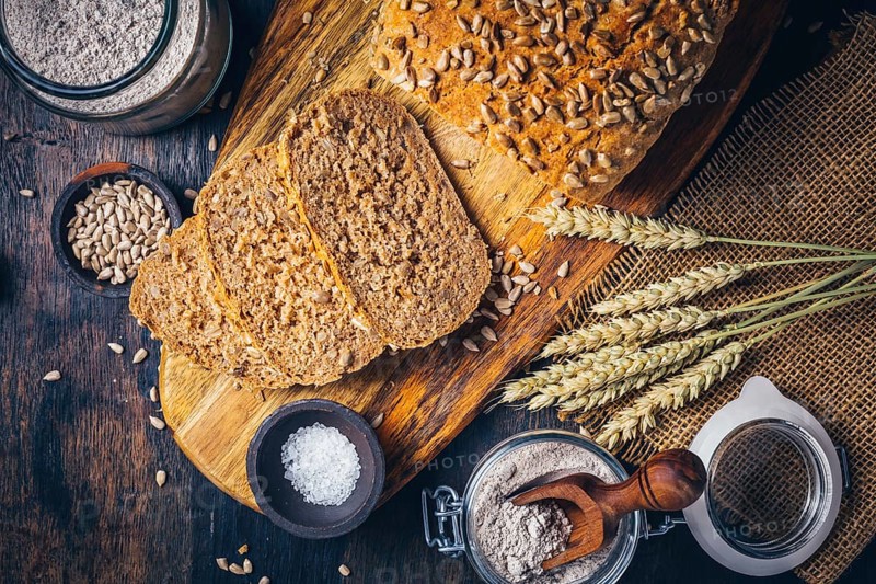 Homemade wholemeal spelt bread with sunflower seeds and baking ingredients on wooden background