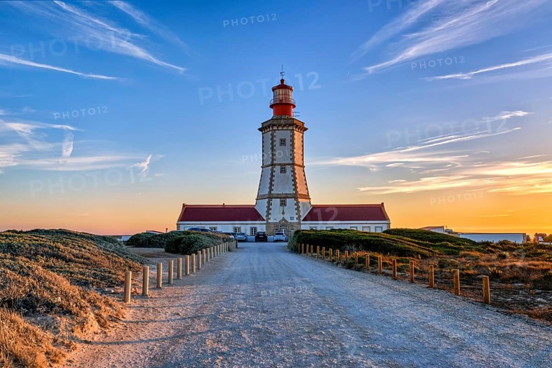 Beautiful of coastal lighthouse in warm colors of sunset, a clear path leading to it. Clear blue sky and some clouds, sun down over horizon, tranquil scene. Navigation beacon, safety for ships and small vessels, Atlantic ocean coast landscape