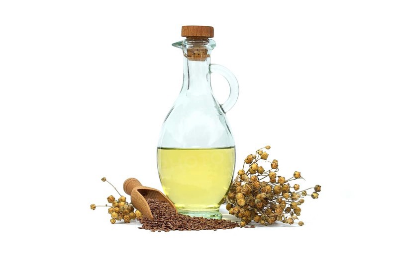 Linseed oil in glass decanter and linseed in wooden scoop near bunch of flax plants isolated on white background. Linum usitatissimum (Common Flax)