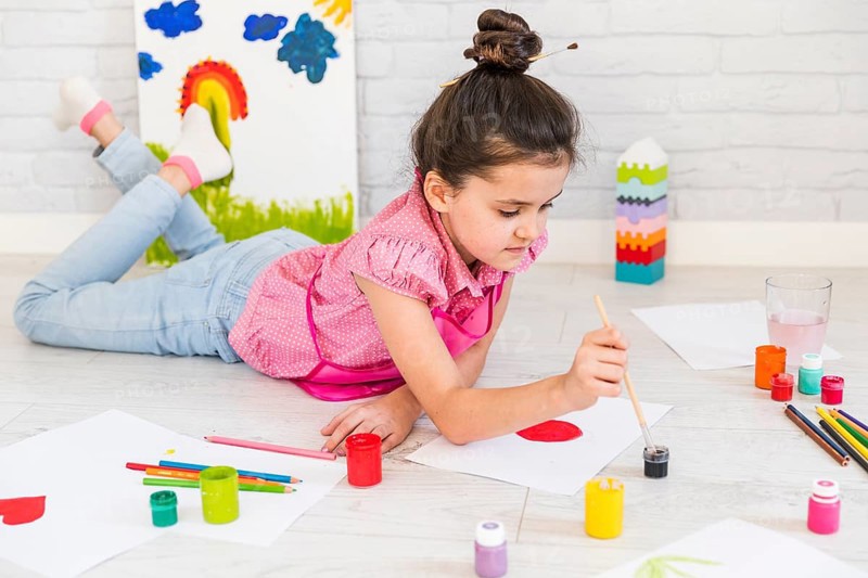 Little girl lying floor painting with water color with paint brush paper