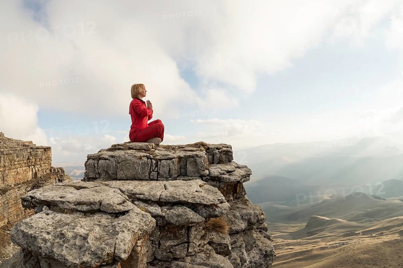 A beautiful girl meditates in a lotus pose sitting on a rock above the clouds against the backdrop of the setting sun and sunset
