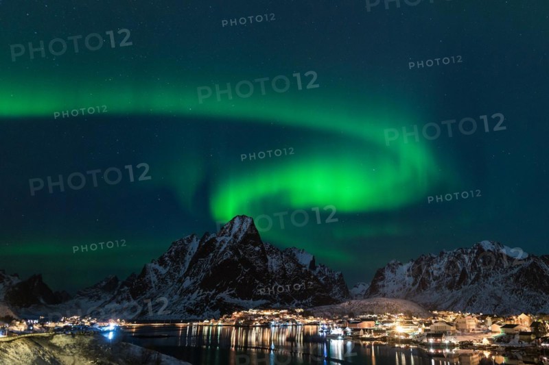 Dancing green polar lights over the village Reine on the Lofoten islands in Norway at night in winter with snow capped mountains