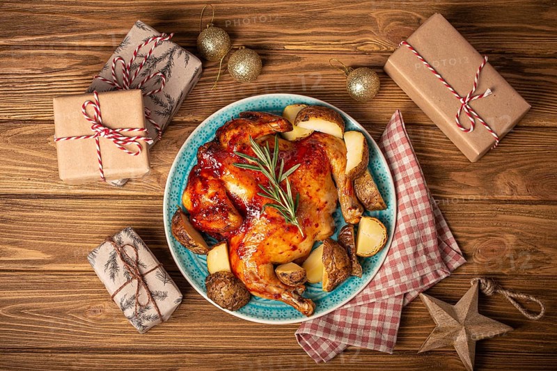 Festive Christmas dinner with roasted whole chicken top view on wooden rustic background with Xmas toys and wrapped presents, festive table composition flat lay