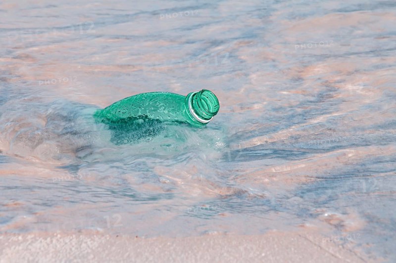 A green plastic bottle floating in the clear ocean water, indicating pollution