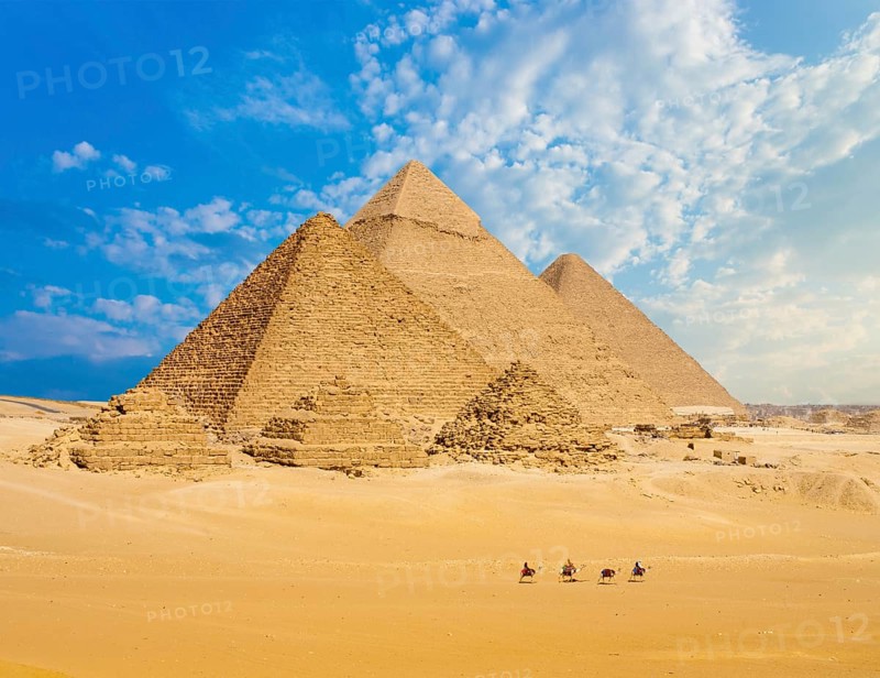 All Egyptian Pyramids from distance with row of camels walking in foreground in Giza, Cairo, Egypt. Wide telephoto shot plenty of copy space